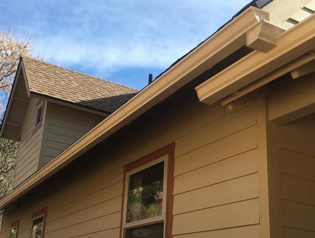 Close-up seamless gutter installation on tan siding